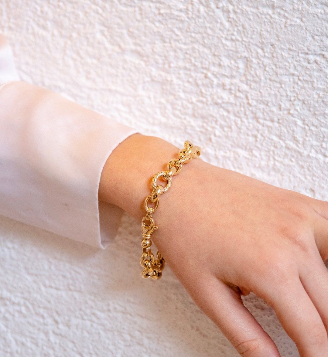 Chunky round-link gold chain bracelet on a wrist against a white wall