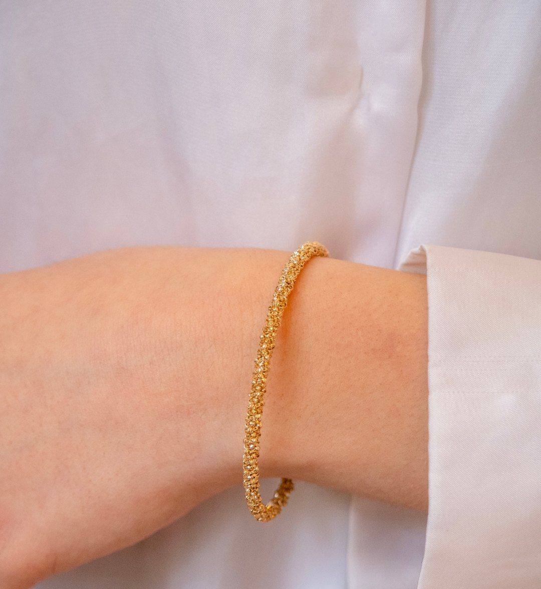 Slim textured round yellow gold bangle on a wrist beside a white shirt cuff