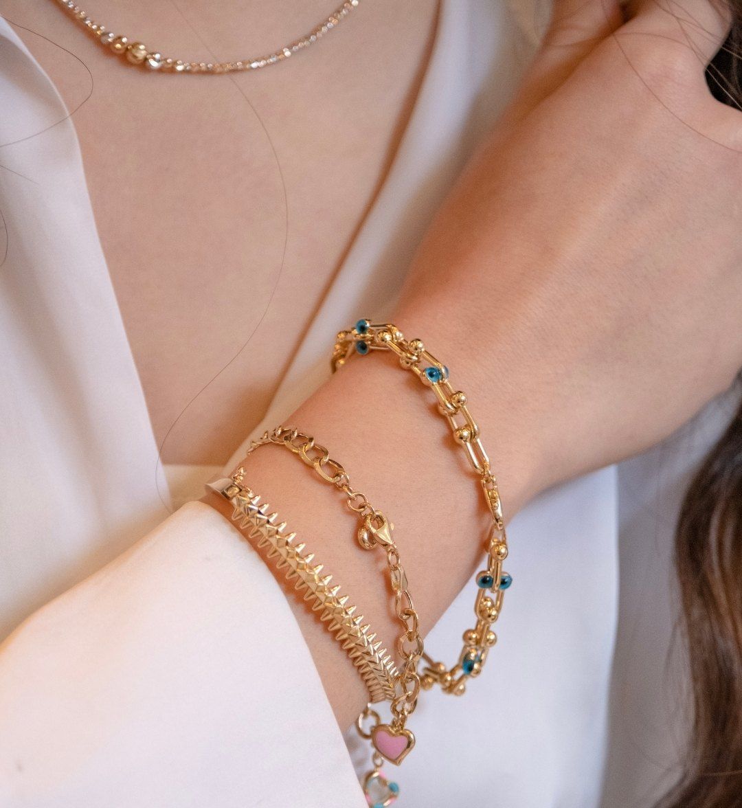 Stacked gold bracelets with blue beads, a herringbone chain and a heart charm on the wrist