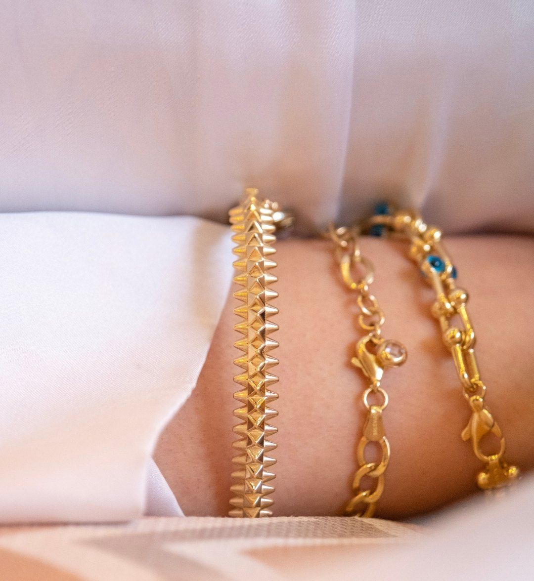 Spiked gold bracelet stacked with a fine chain and a blue-beaded bracelet, close-up
