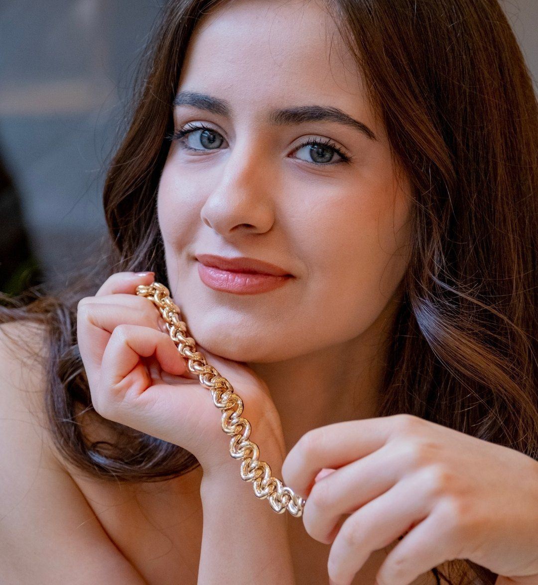 Chunky linked gold chain bracelet held up by a model near her chin