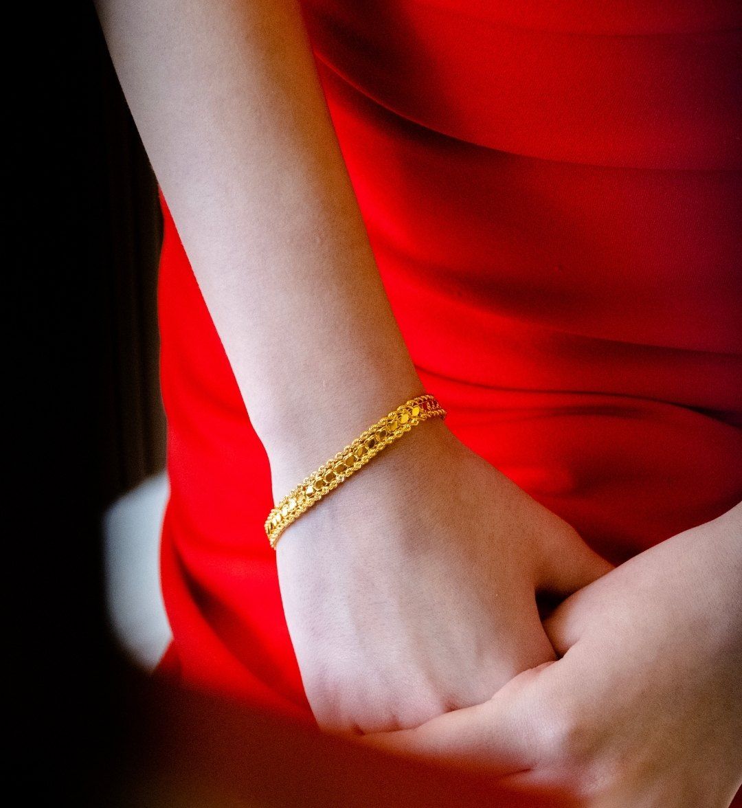 Engraved band-style gold bracelet on a wrist against a red dress