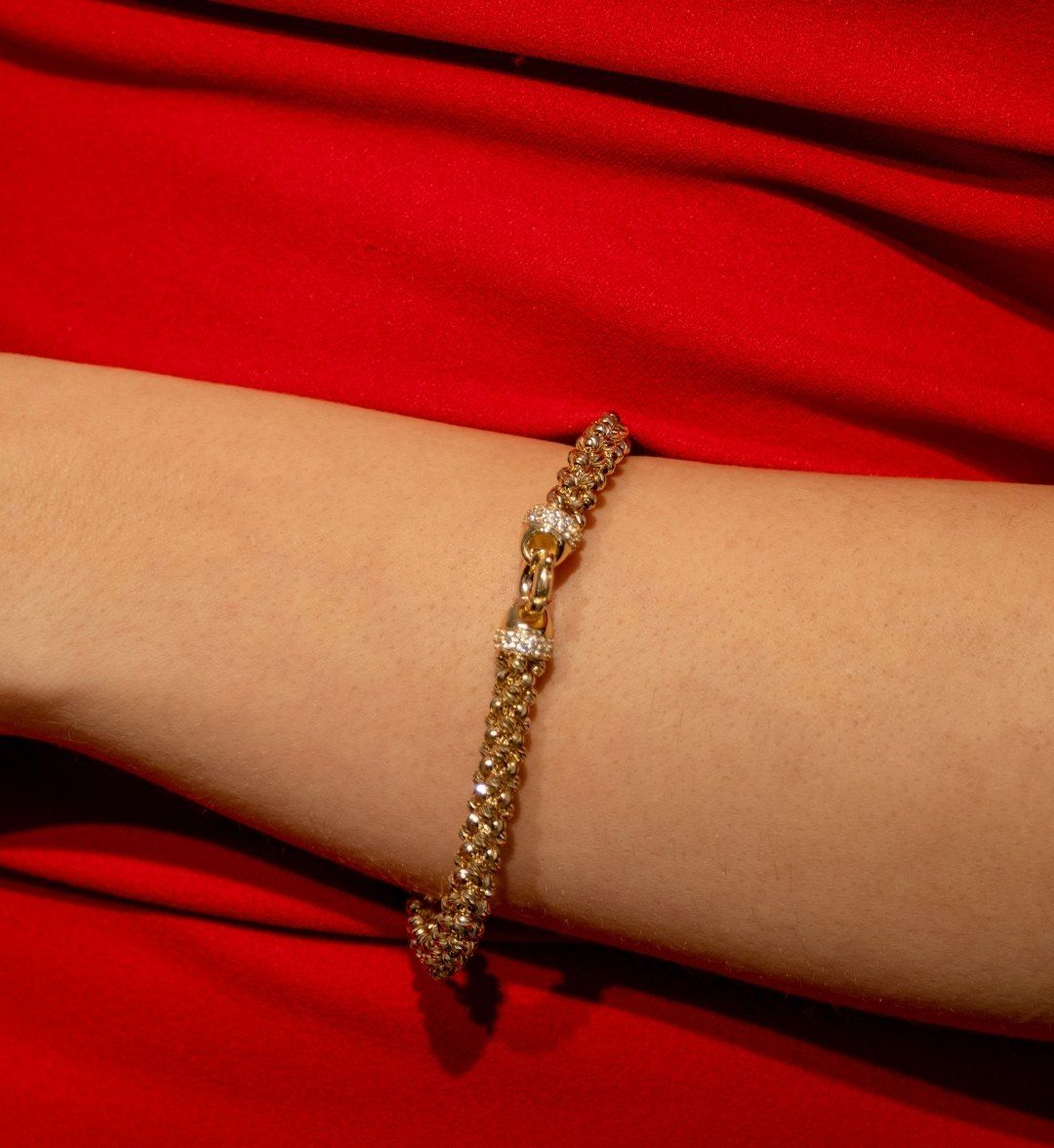 Dense woven gold bracelet with stone-set clasp detail on a wrist over red fabric