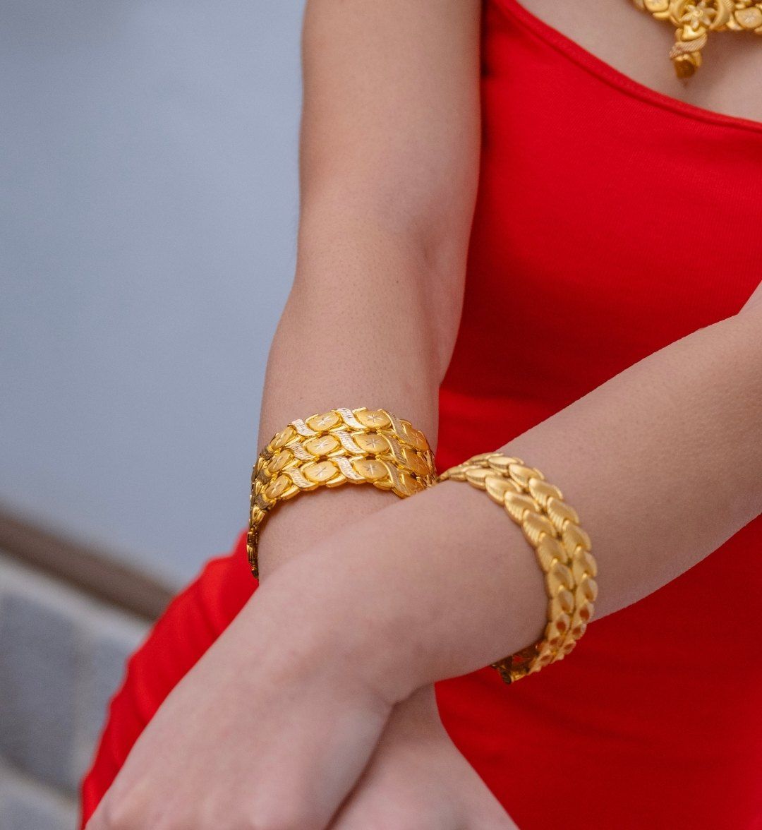Wide leaf-woven gold cuffs on both wrists of a model in a red dress