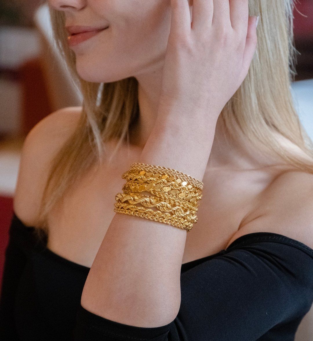 Many twisted and textured gold bangles stacked high on a model's wrist