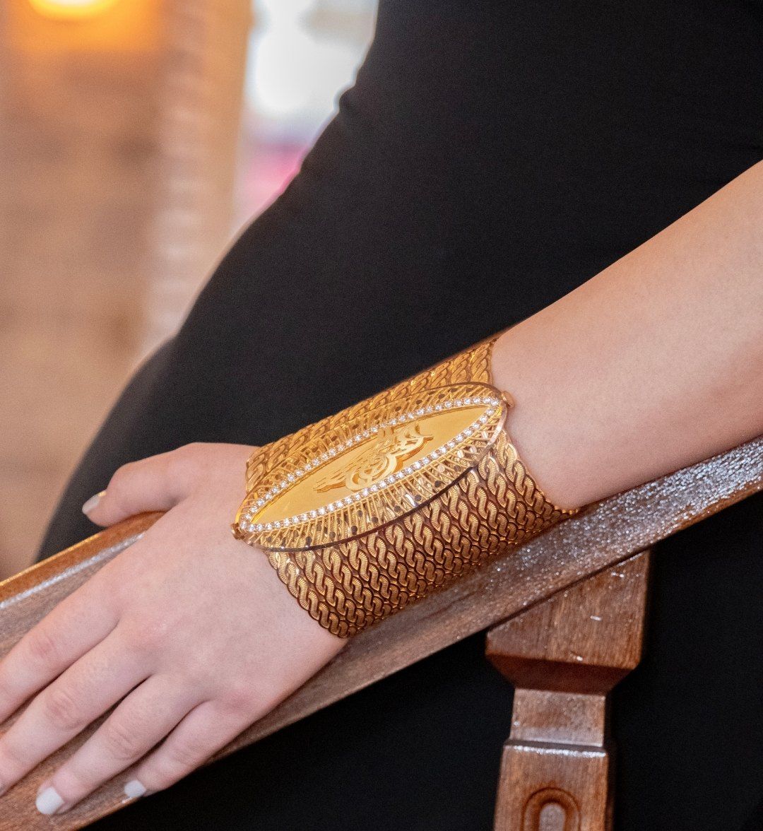 Wide woven gold cuff with an engraved oval plate bordered by small stones on the wrist