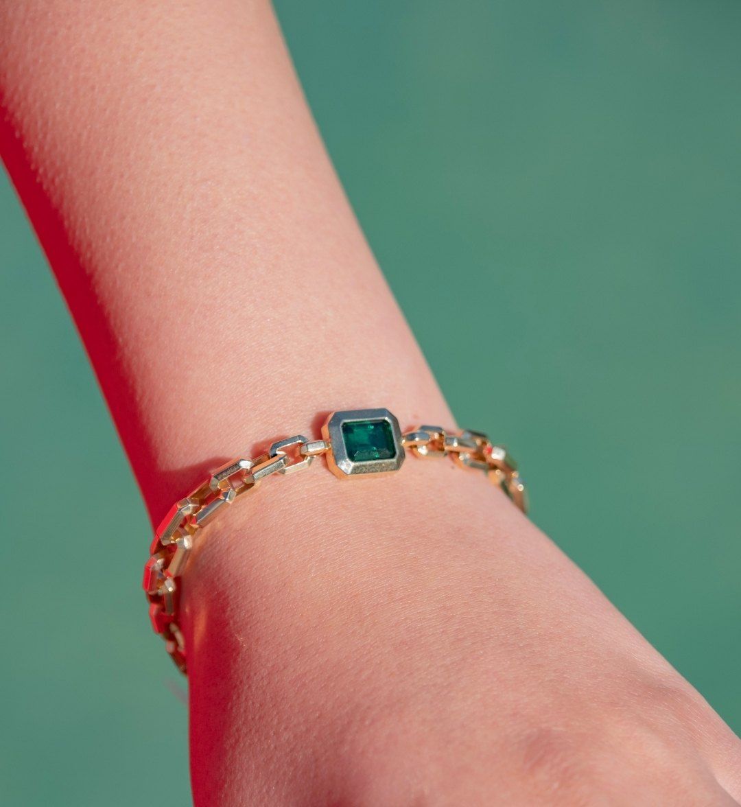 Chunky linked gold chain bracelet with a square green stone on the wrist