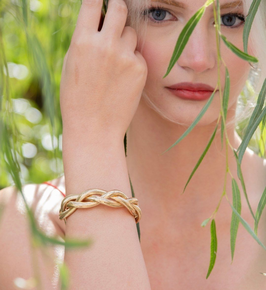 Braided yellow gold bracelet on a model's wrist, framed by willow branches