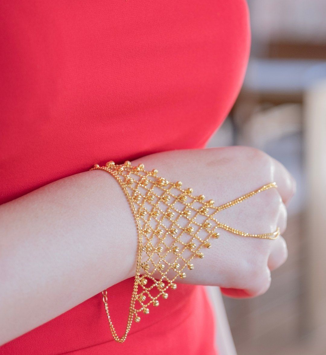 Gold mesh hand chain with tiny gold beads on a model's hand, linked to the fingers