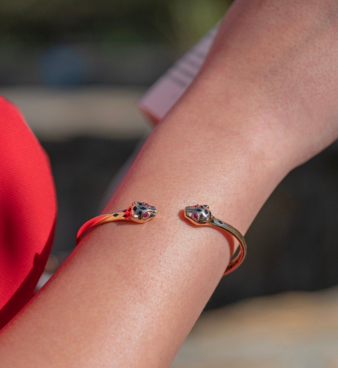 Open gold cuff with panther-head ends, red stone eyes and black enamel, worn on the wrist