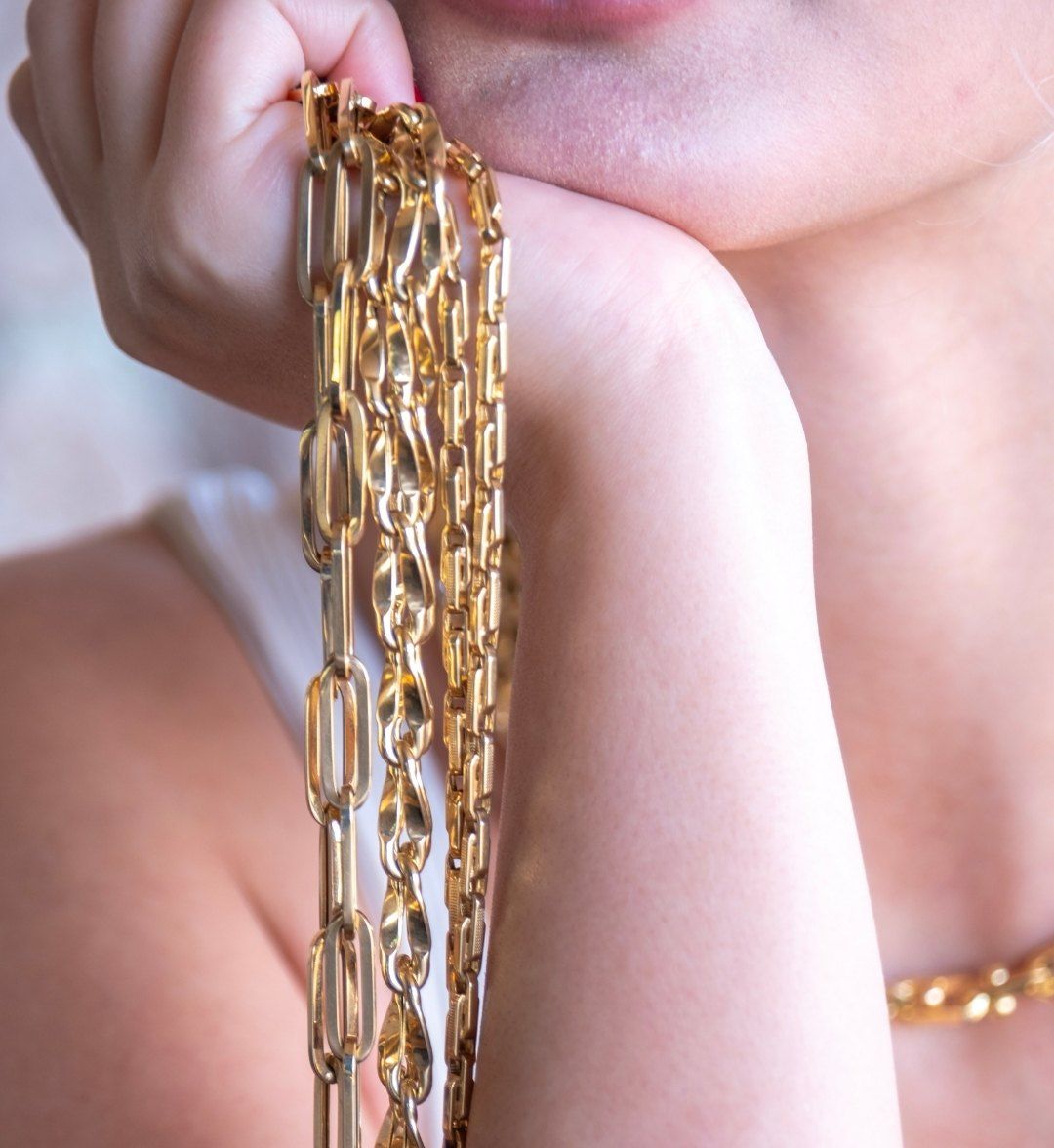 Several long gold chains in different link styles hanging from a model's hand, close-up