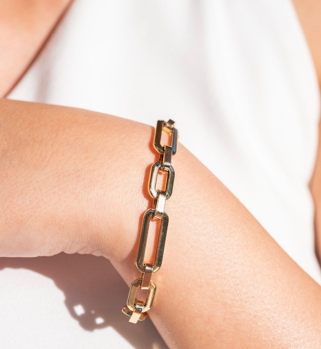 Polished yellow gold rectangular-link chain bracelet on an arm in sunlight, close-up