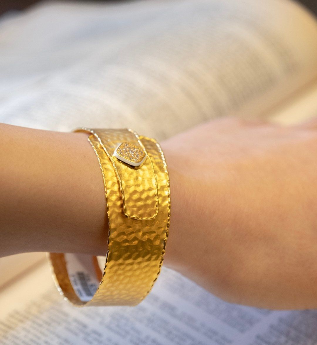 Wide hammered yellow gold cuff with a square white stone-set plate, worn on the wrist