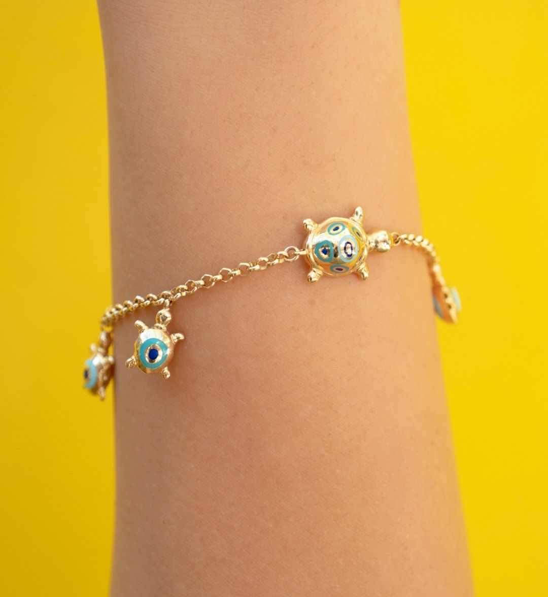 Gold charm bracelet with dangling turtle figures and blue enamel evil-eye motifs, on the arm