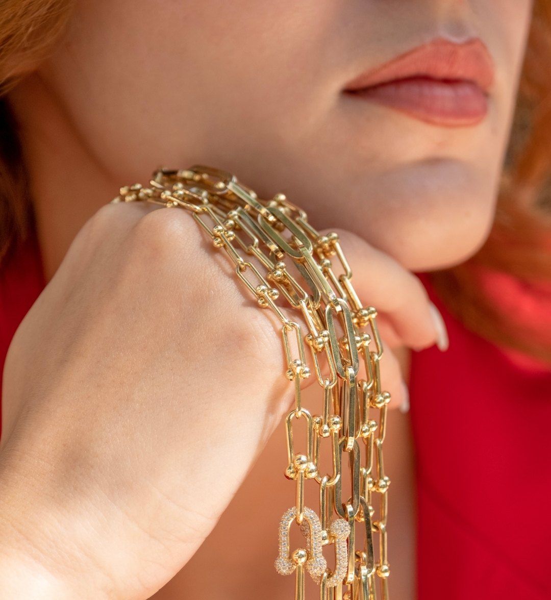 Gold chains with ball-accented links and a white stone-set clasp draped over a hand