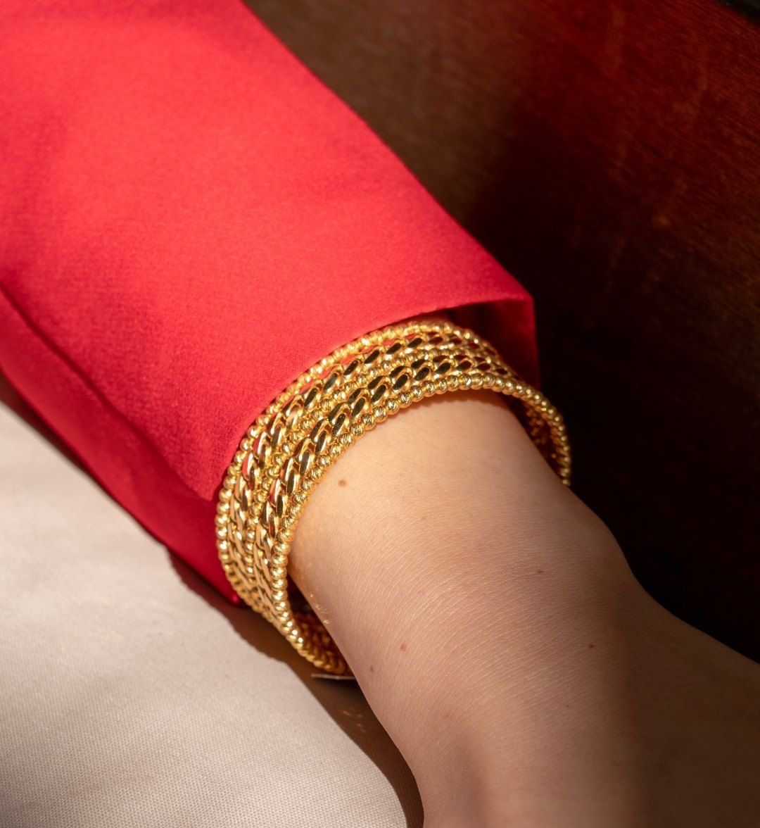 Stacked yellow gold bangles in twisted and beaded designs below a red sleeve