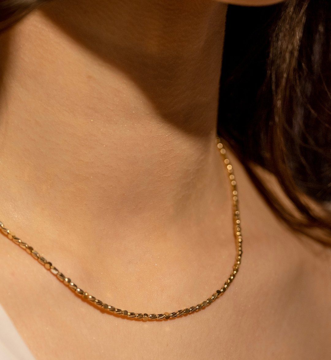 Fine beaded-texture yellow gold chain necklace on the neck in warm light, close-up