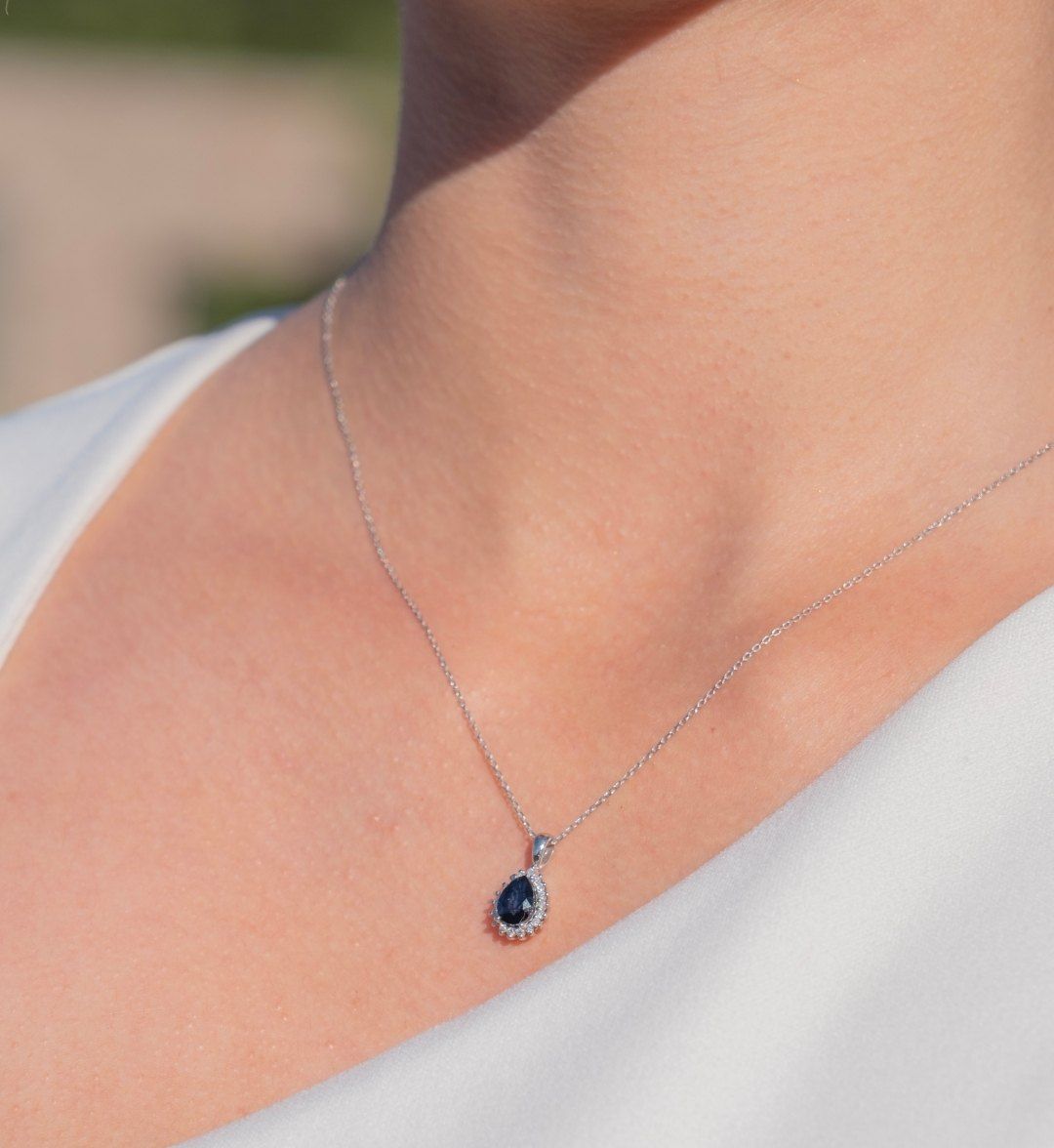 Navy stone teardrop pendant ringed with white stones on a white gold-tone chain