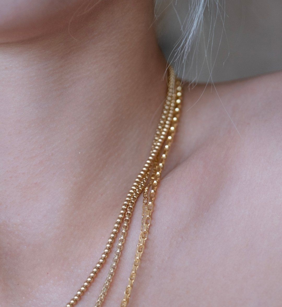 Layered fine gold necklaces in ball and box chain on the neck, close-up