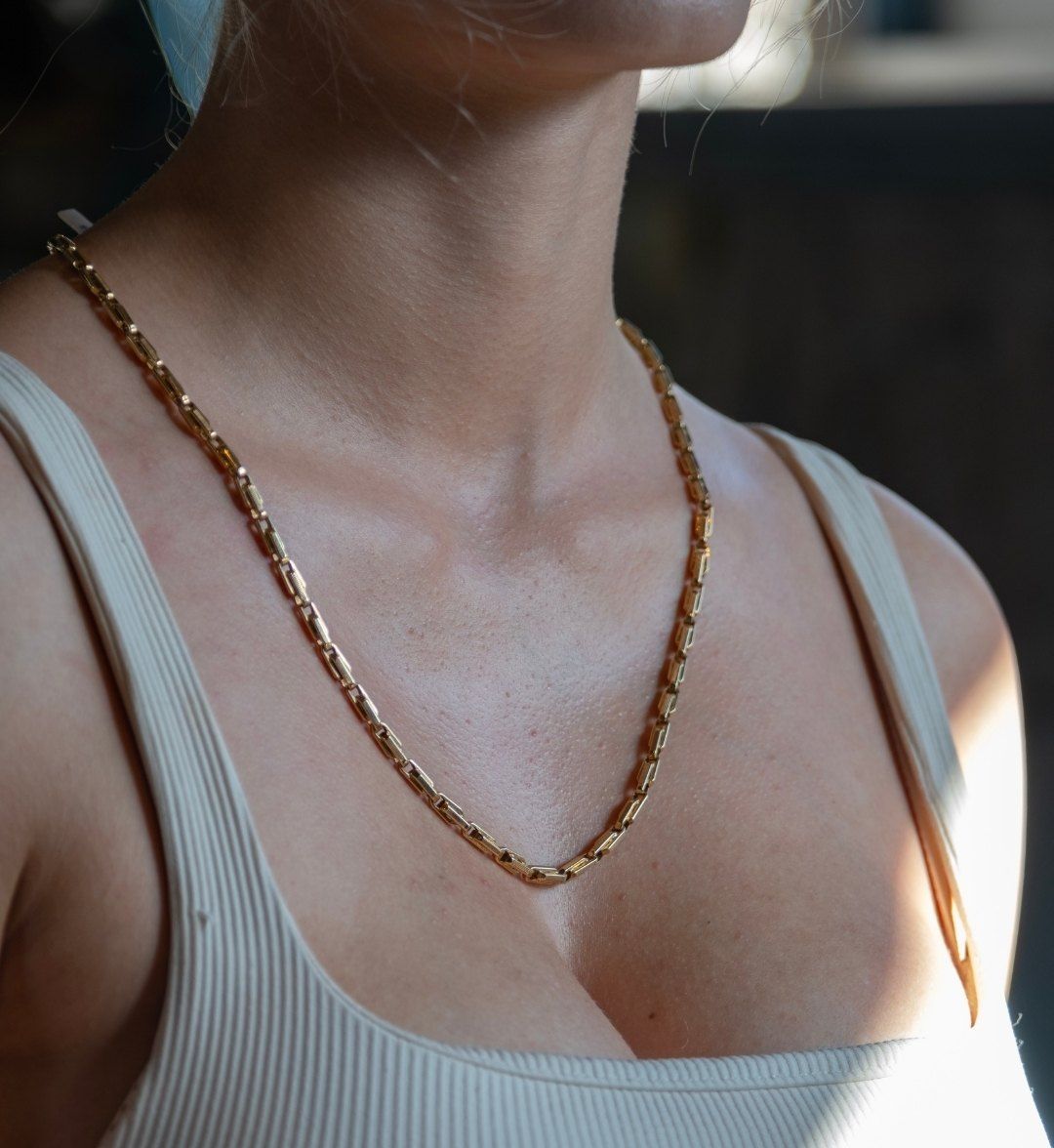 Yellow gold rectangular-link chain necklace on the décolletage in side light