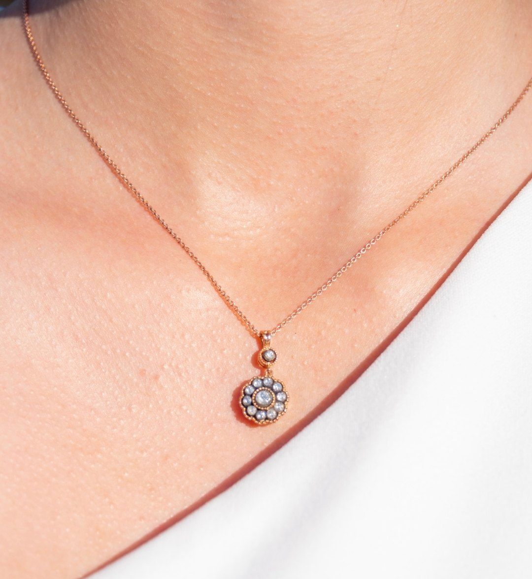 Flower-motif pendant with grey and white stones on a rose gold chain, worn on the neck