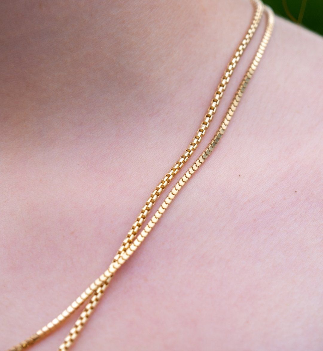 Two strands of fine gold box chain resting on the collarbone, close-up