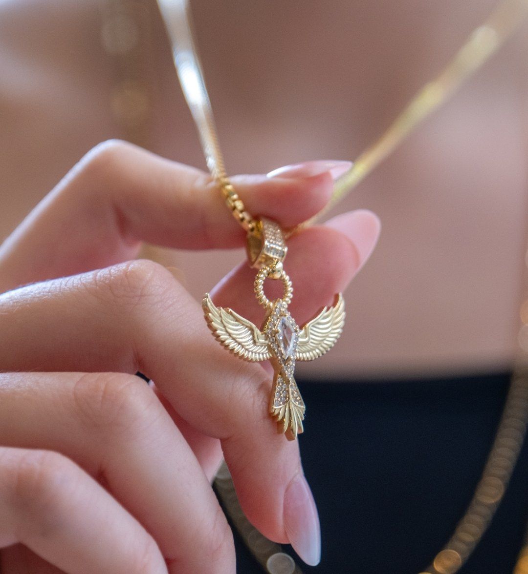 Winged bird gold pendant set with white stones, held between the fingers