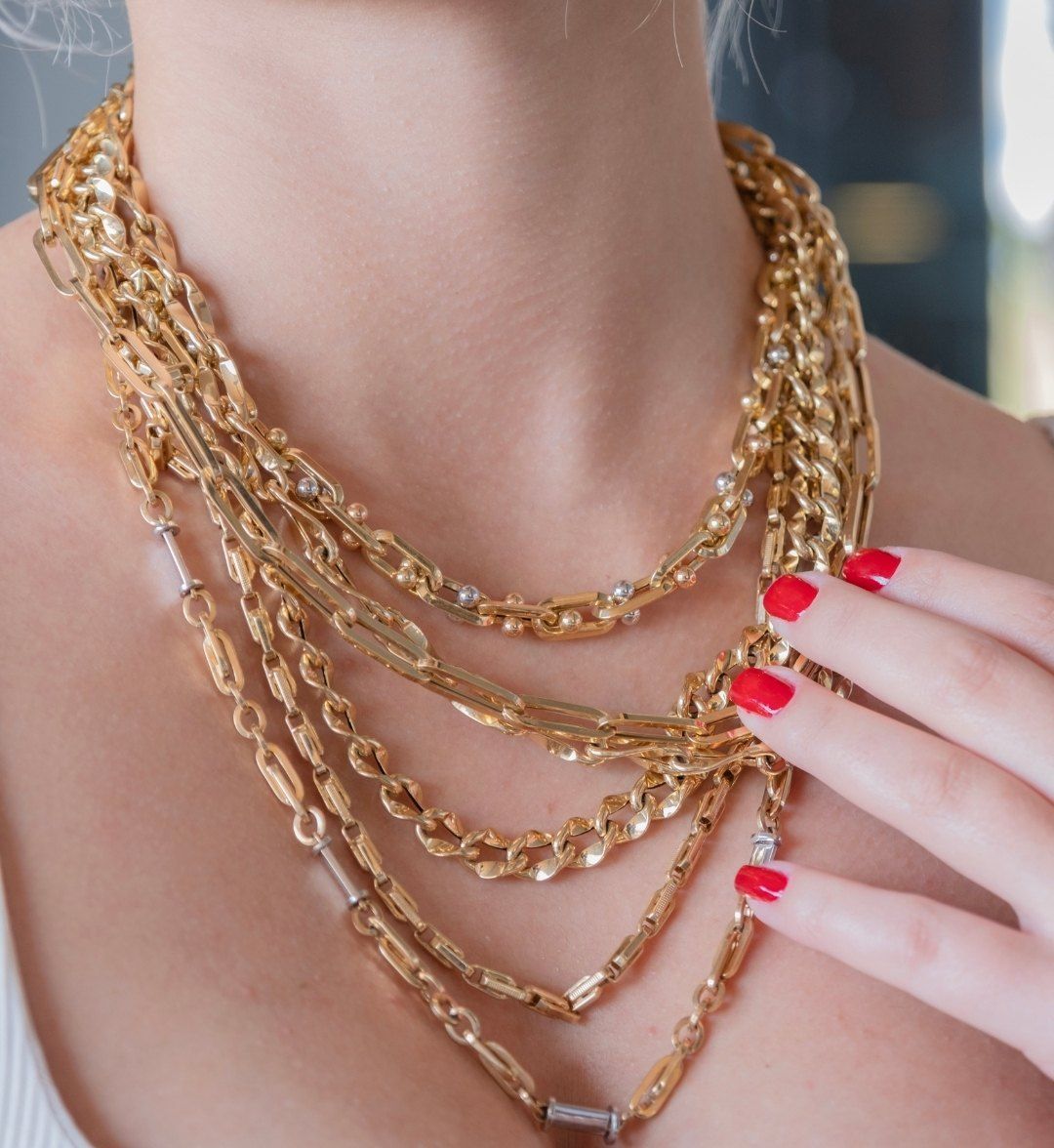 Multiple chunky yellow gold chain necklaces in mixed links layered on the neck
