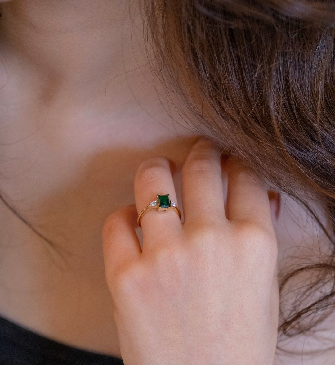 Gold ring with a green rectangular stone flanked by white baguette stones on a hand