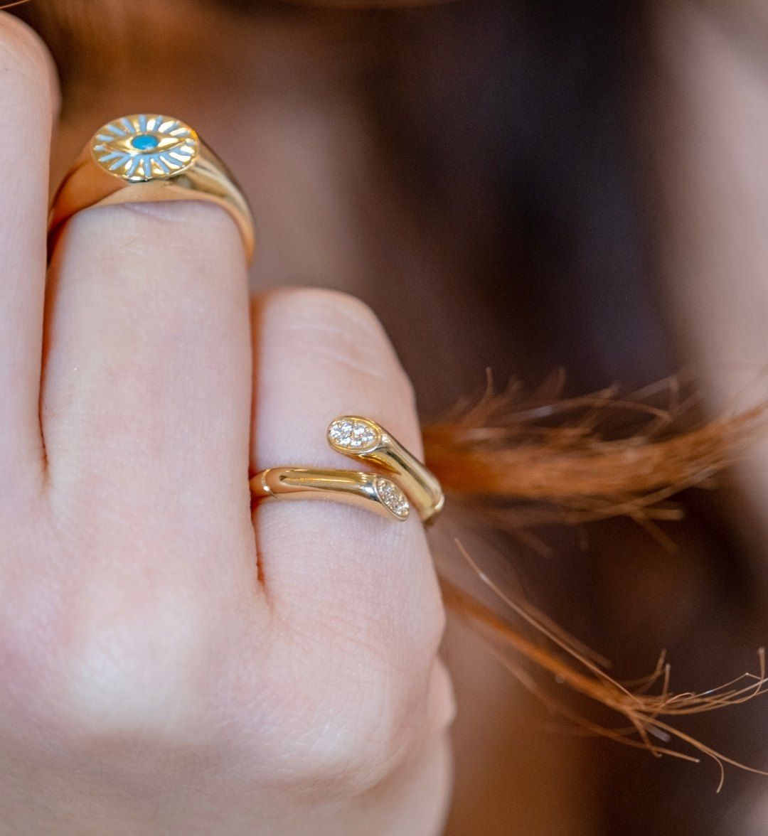 Gold signet ring with a blue enamel eye motif beside an open ring with white stones