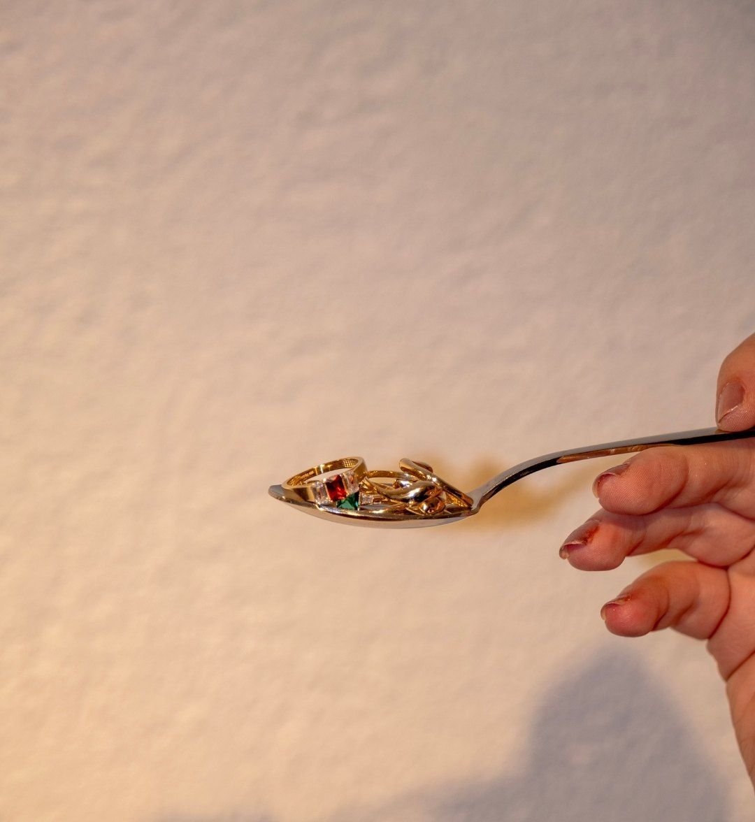 Several yellow gold rings in a spoon, including one with red and green stones