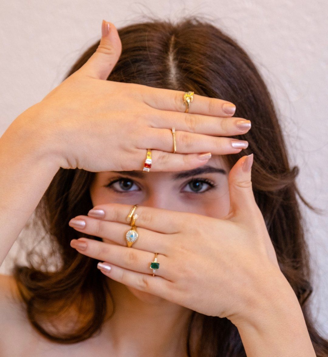 Stone-set, signet and slim band gold rings on both of a model's hands framing her face
