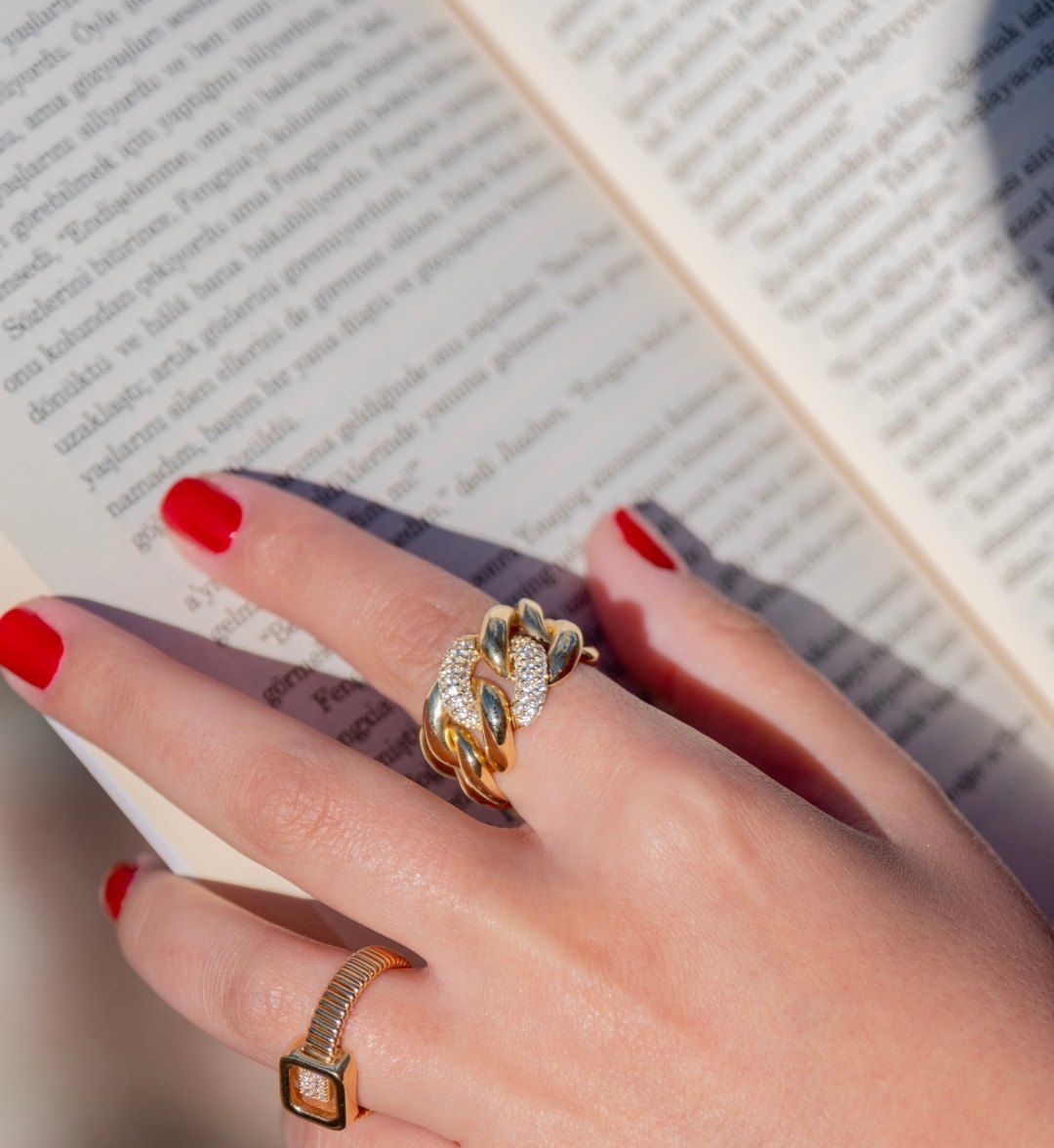 Chunky chain-link ring with white stones and a square stone-set ring on a hand over a book