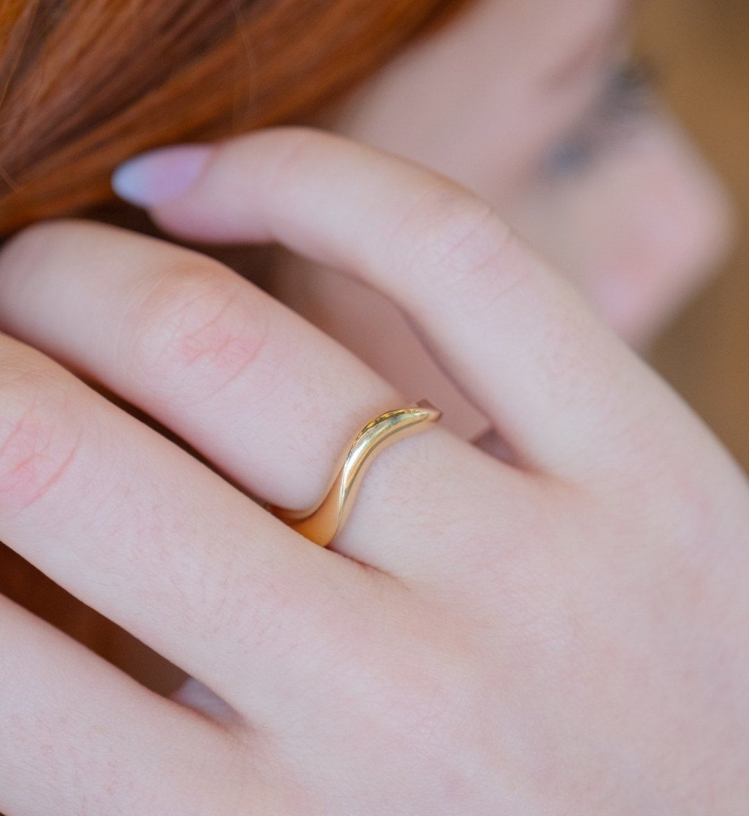 Plain yellow gold ring with a gentle wave shape on a finger, close-up