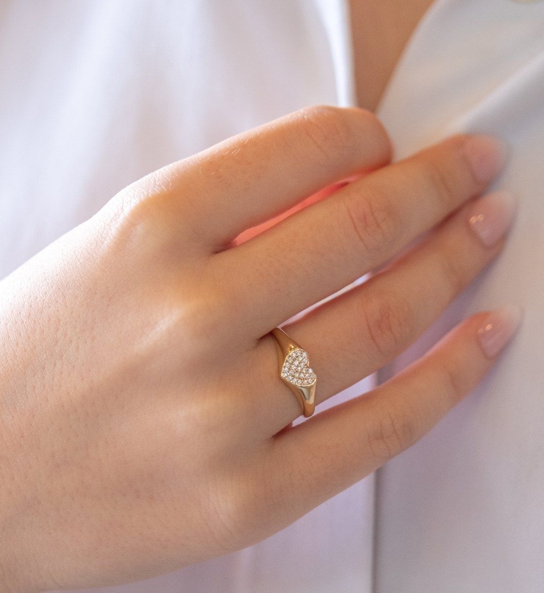 Gold signet ring with a heart-shaped face covered in white stones on a hand