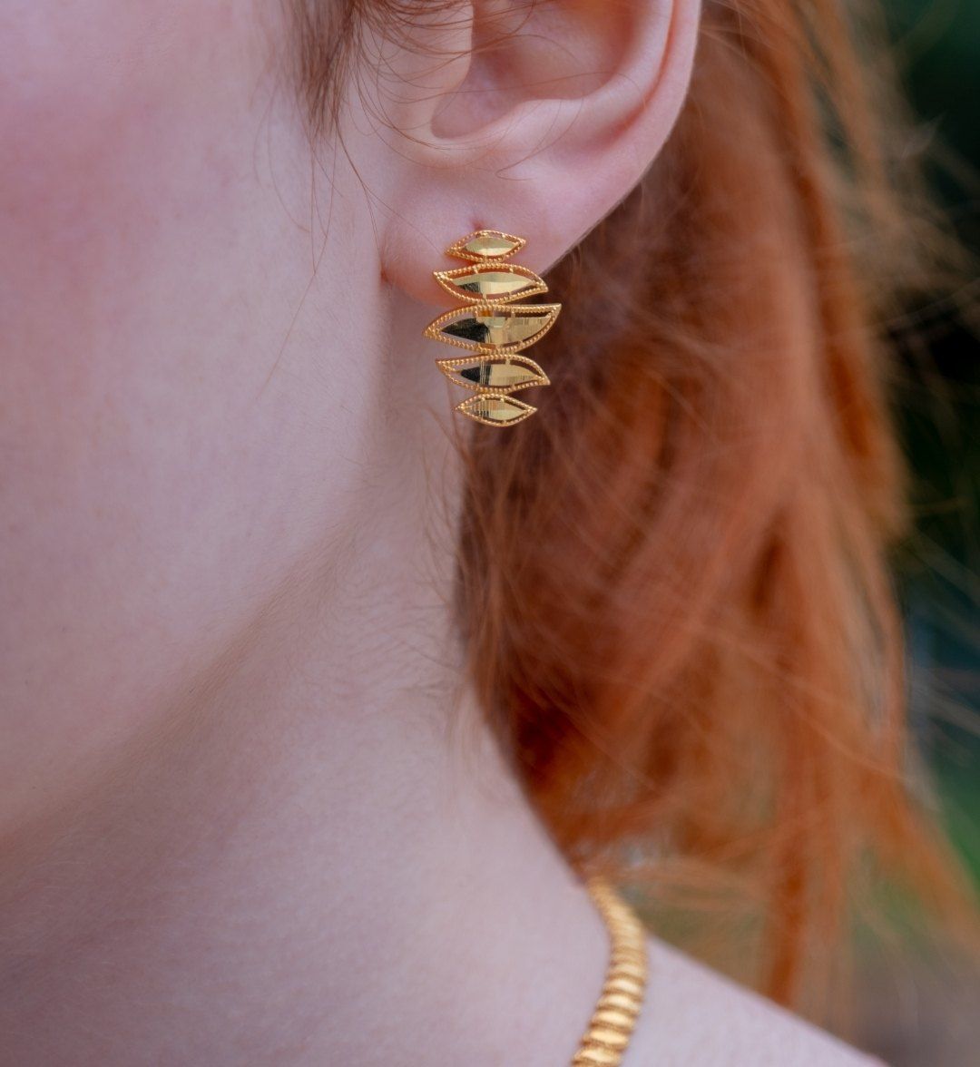 Gold earring of stacked leaf shapes worn on the ear, close-up