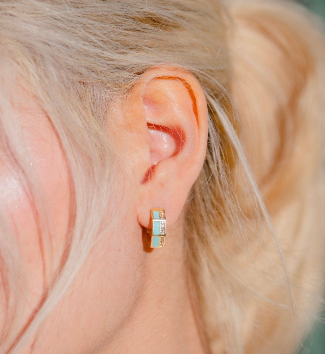 Small gold hoop earring with turquoise and white stones on the earlobe, close-up