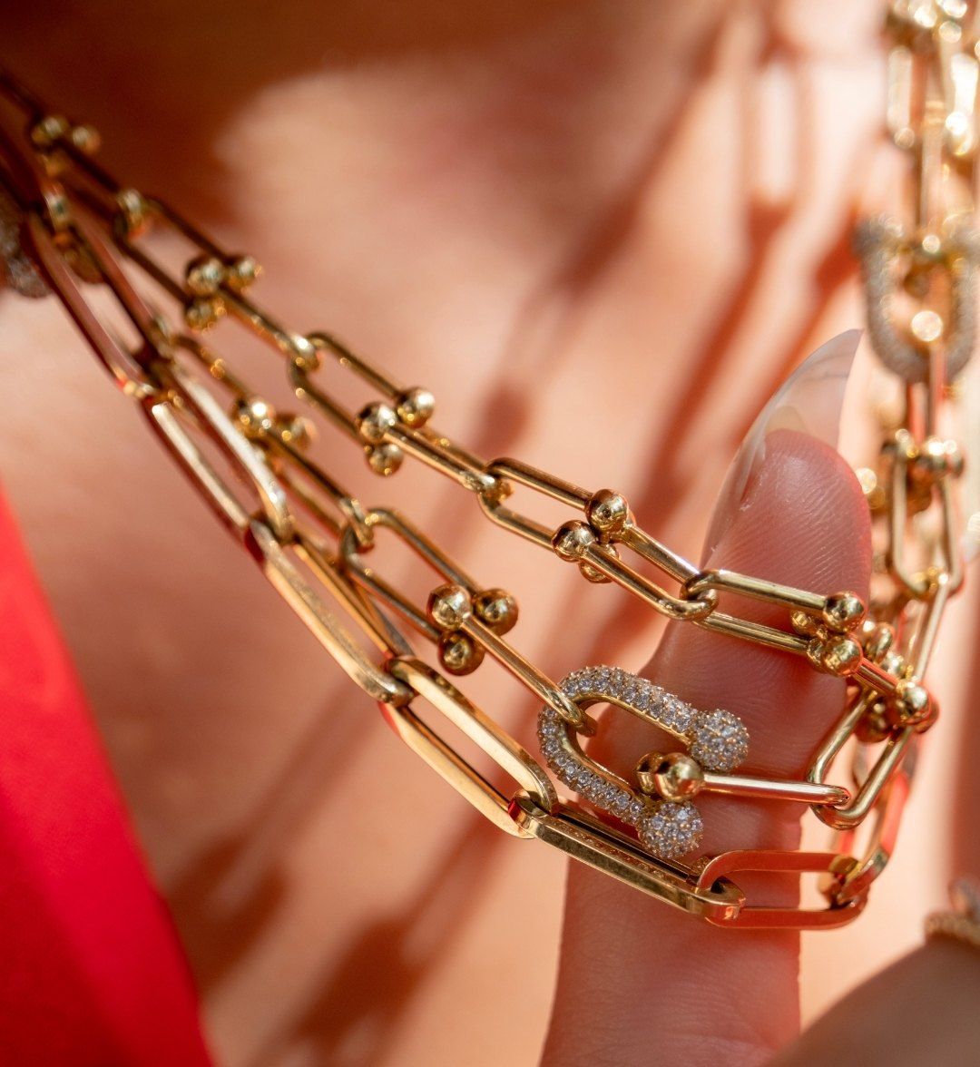 Paperclip and ball-link chain necklaces gathered on a finger, with a white stone-set clasp