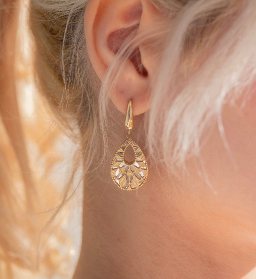 Open teardrop earring with engraved yellow and white gold detail worn on the ear