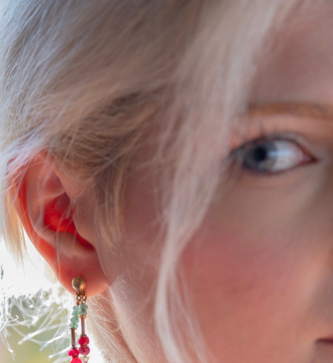 Gold drop earring with green and red beads on the ear, close-up beside the face