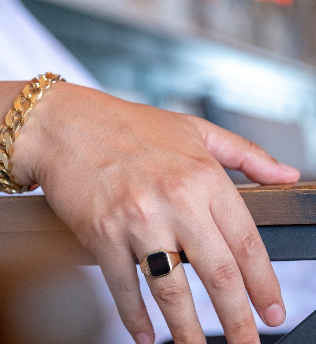 Gold signet ring with a black stone on a man's hand, with a chunky chain bracelet