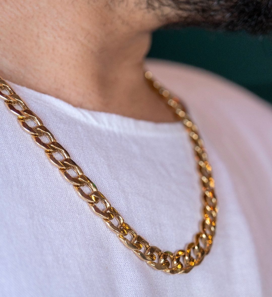 Chunky curb-link men's gold chain worn over a white T-shirt, side close-up