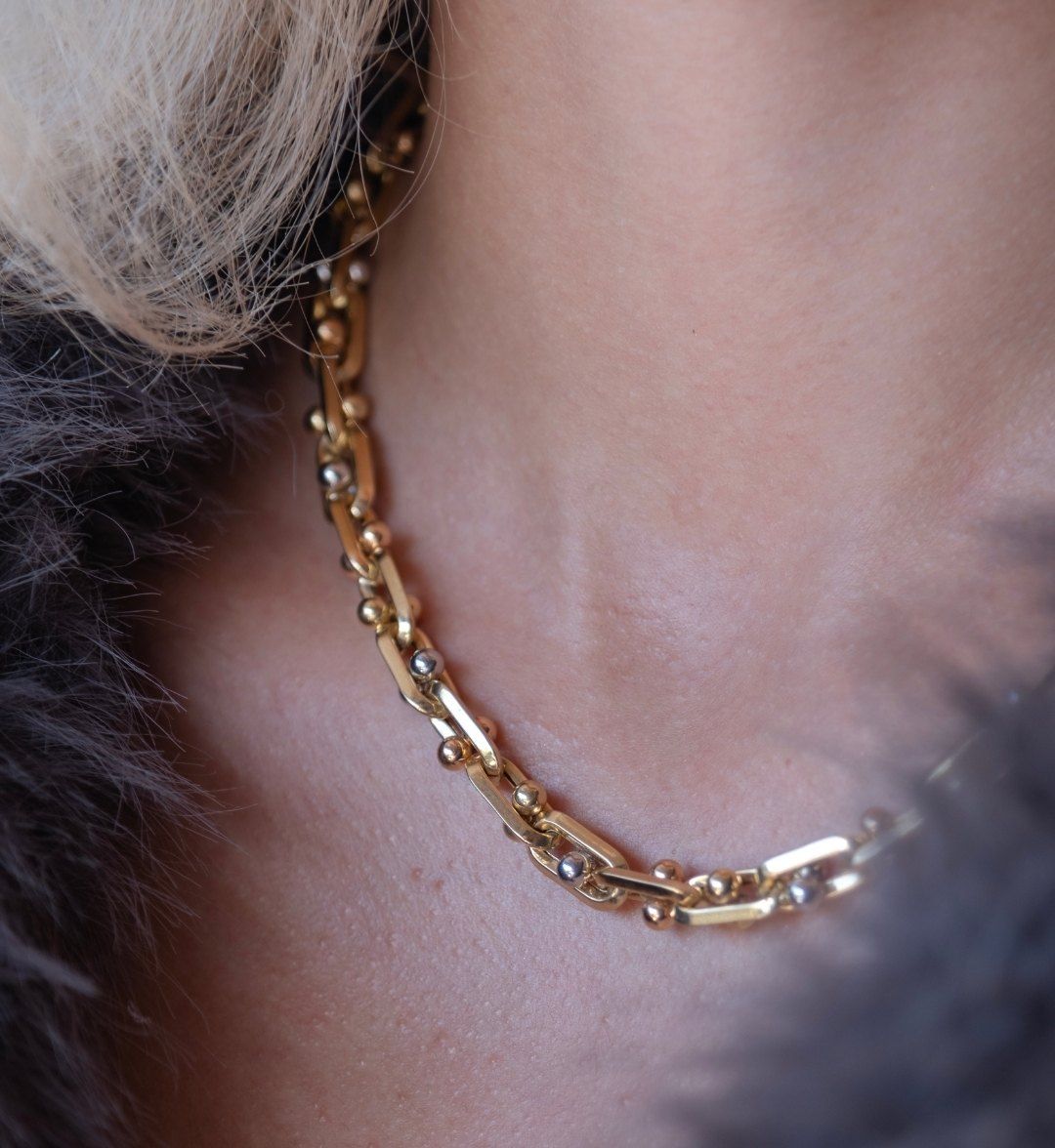 Fancy link necklace of long links joined by gold balls, worn on the neck beside a fur collar