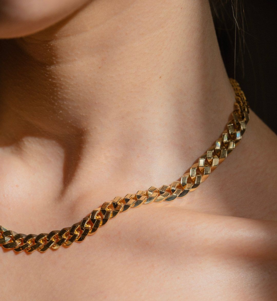 Flat, polished curb chain necklace along the neck and collarbone, close-up