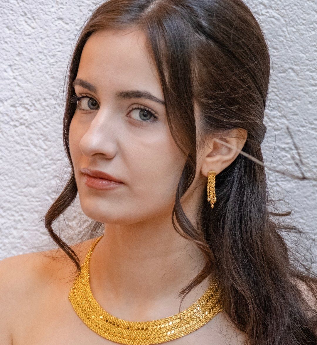 Portrait of a model wearing a wide woven gold collar with a matching woven drop earring