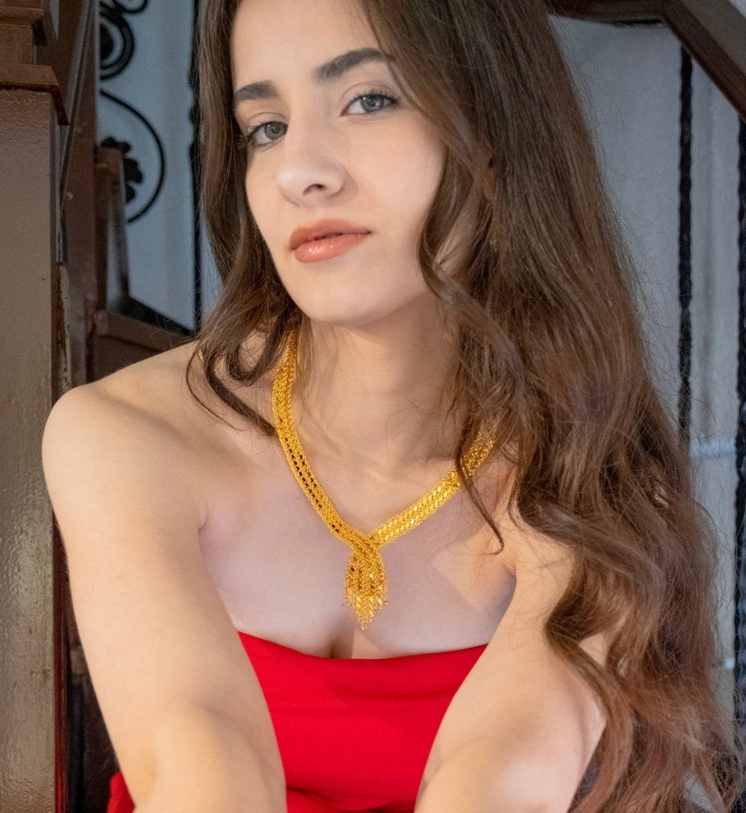 Woven gold collar necklace with a tie-style drop, worn by a model in a red dress