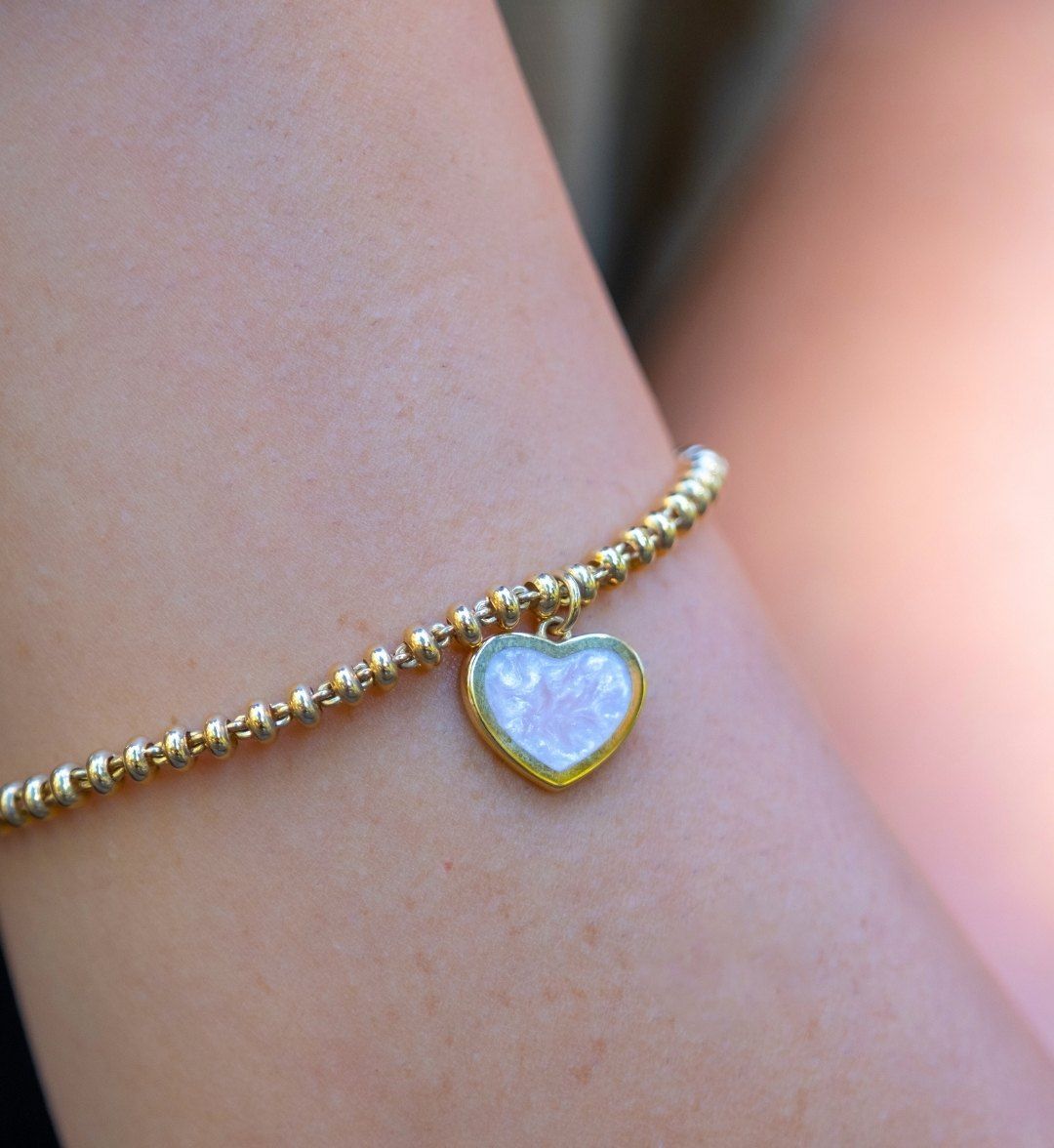 Pearly white heart charm on a fine gold beaded bracelet, close-up on the arm