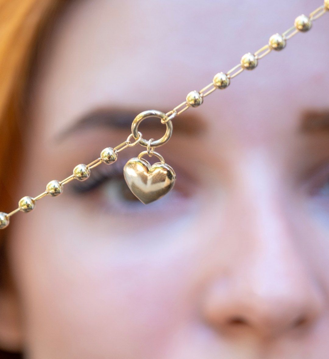 Heart pendant necklace with a puffed gold heart on a ball chain, held up close to the camera