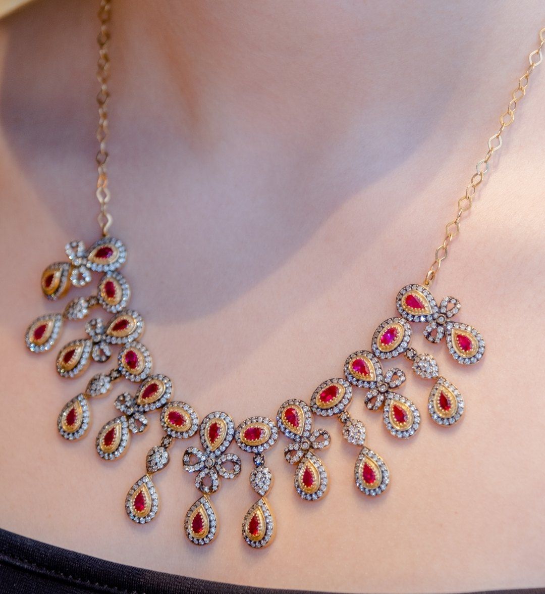 Statement necklace of pear-cut red stones framed in white stones with bow motifs, close-up