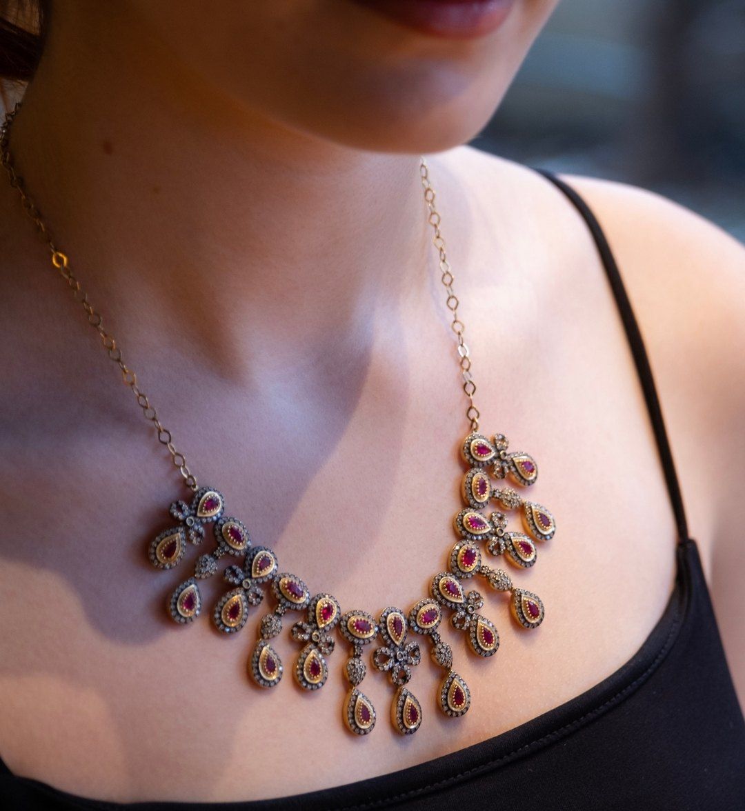 Antique-look necklace with red teardrop stones worn by a model in a black strappy top